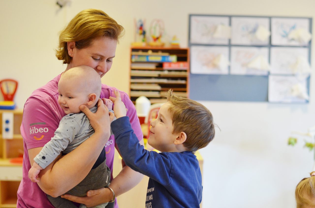 Kibeo kinderverzorgster houdt baby vast in bijzijn van kleuter